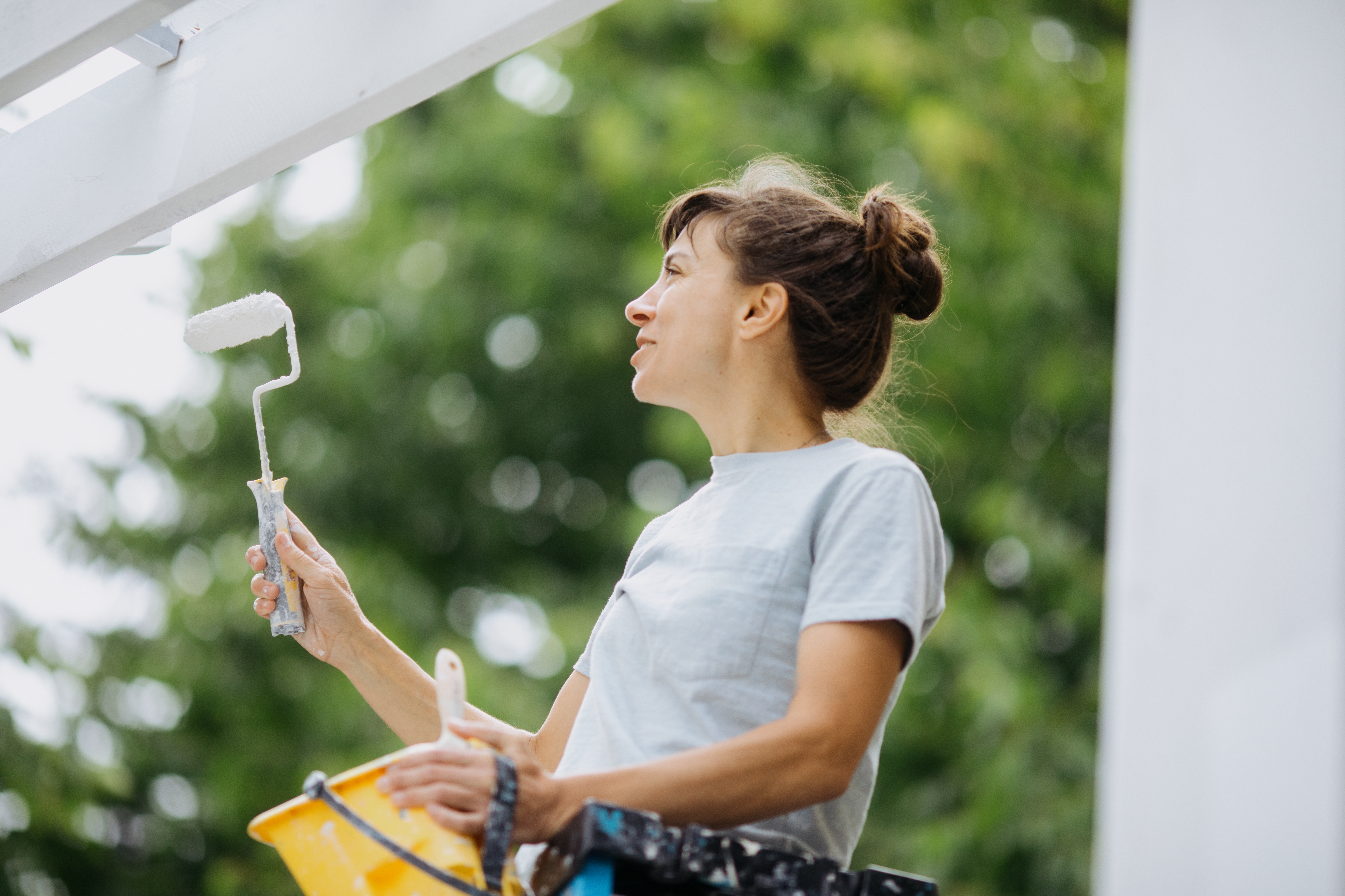 Woman painting house deck with paint brush and bucket